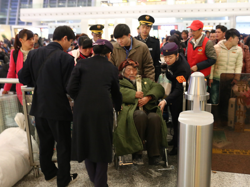 检票口，工作人员在提前验票后打开了应急通道，方便老人通过，工作人员围了过来，帮老人推车、拿行李。乘客们也自觉的让出了一条通道。