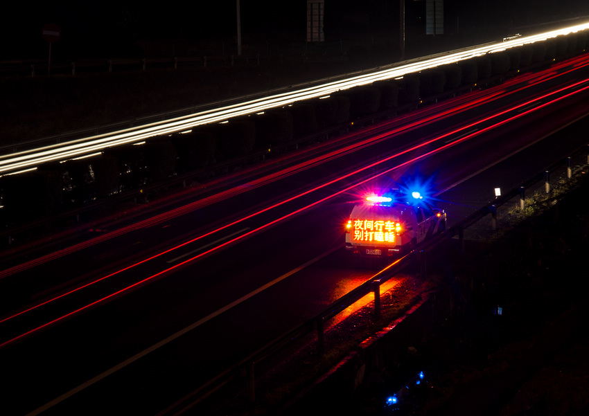 夜深了，一辆警车和来去的车辆灯光拖长的轨迹。姜豪 摄