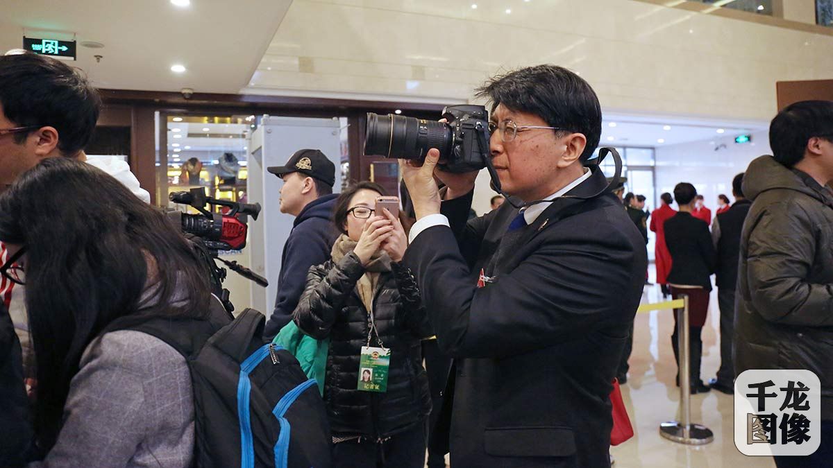 1月20日，政协委员朱良在接受记者采访的同时也不忘拍下身边的精彩瞬间。千龙网记者 王璟玥摄