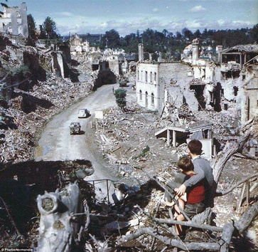 22. 诺曼第战役之后两位男孩看美军士兵驾车开过法国圣洛（Saint Lo）。
