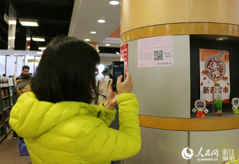 一位市民正在扫描墙上的“悦读服务”二维码，下载APP。