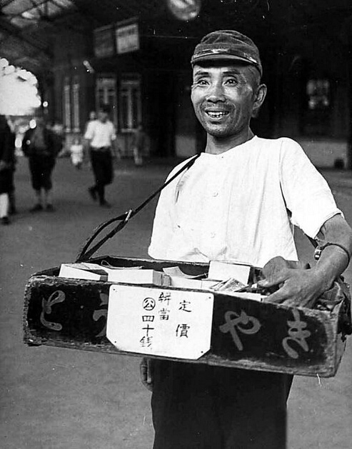 这不是日本兵，是个戴着那时盛行的帽子的小贩。又可以平平安安做生意了，当然充满喜悦。他卖的盒饭，也叫便当。他此时充满信心，在人声嘈杂的火车站，这些会很快销完的。