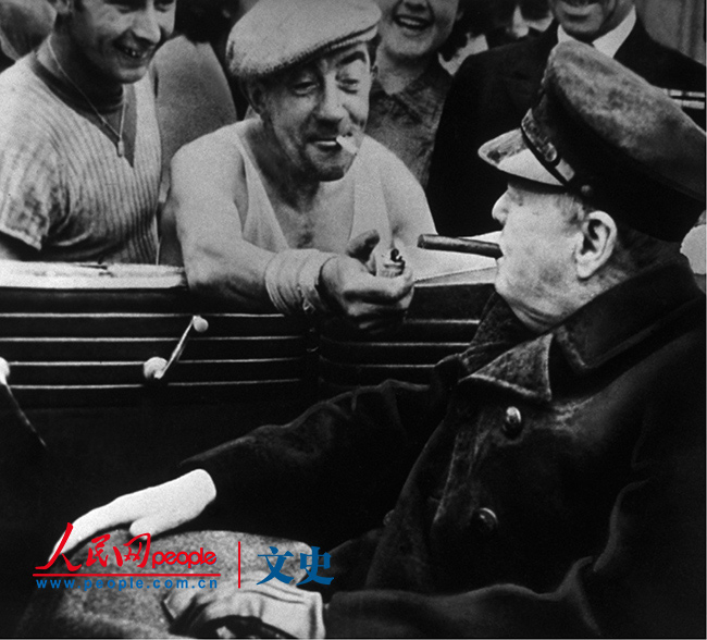 【1940年代】瑟堡的一名码头工人给丘吉尔点烟。1944年6月，盟军反攻登陆数日后，英国首相访问这个法国港口残存的部分。盟军围攻持续一周，该城始获自由。