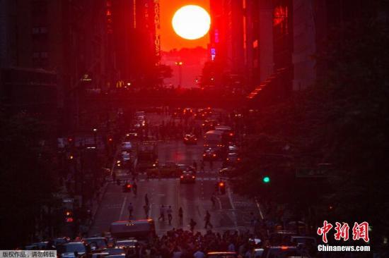 资料图：当地时间7月11日，美国纽约曼哈顿再现“曼哈顿悬日”景观，引得路人纷纷围观。据悉，曼哈顿街道大多呈棋盘布局，每年5月底和7月初各有一天日落时分，太阳会精准地落在两排摩天大楼之间，阳光洒满曼哈顿所有东西向街道，形成壮观的“曼哈顿悬日”，时间长达15分钟。