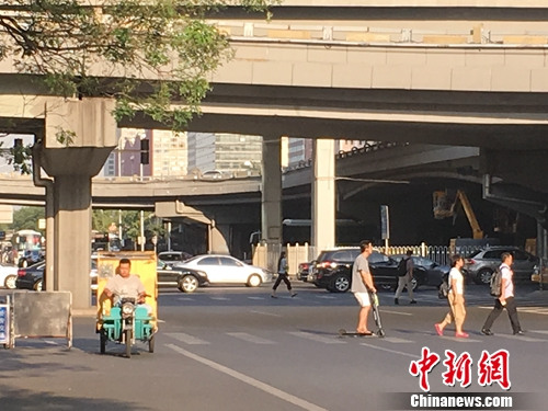 北京国贸附近有人骑电动滑板车过马路。汤琪 摄
