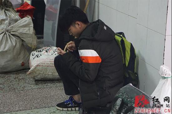 肖雪慧坐在行李箱上候车，拿着手机玩游戏打发时间。