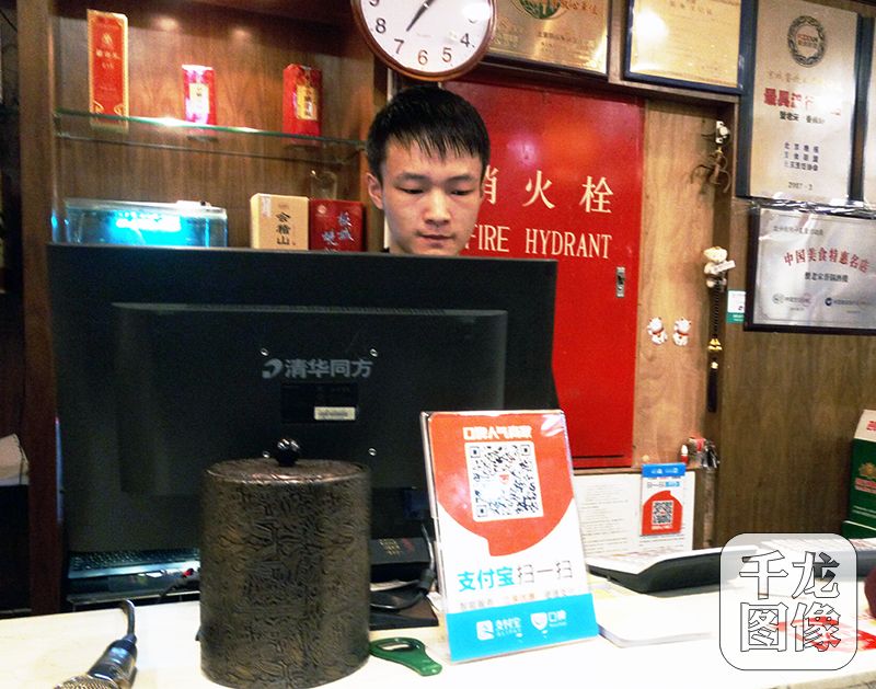 如今，扫码支付已成为潮流，无论是家门口的早点铺、水果摊，还是商场、大超市，都能通过支付宝和微信扫描二维码进行支付。图为餐厅收银台前摆放着支付宝收款的二维码。千龙网记者 查甜甜摄