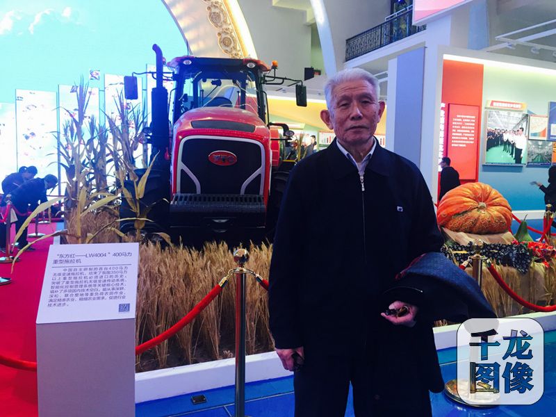 近日,在“砥砺奋进的五年”大型成就展“践行发展理念 引领经济发展新常态”展区,悟空卫星、蛟龙号、复兴号、可燃冰开采设备……一系列上天入地的大国重器模型展示在众人面前,引来不少市民的驻足。图为80岁的范国强老人在“东方红——LW4004”重型拖拉机前合影留念。千龙网记者 欧阳晓娟摄