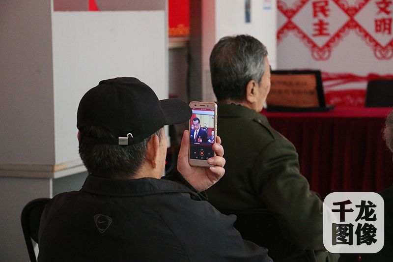10月18日上午，通州区北苑街道新华西街社区的30多位老党员、志愿者共同收看党的十九大开幕式。图为一位居民拿出手机记录开幕式。千龙网记者 马文娟摄