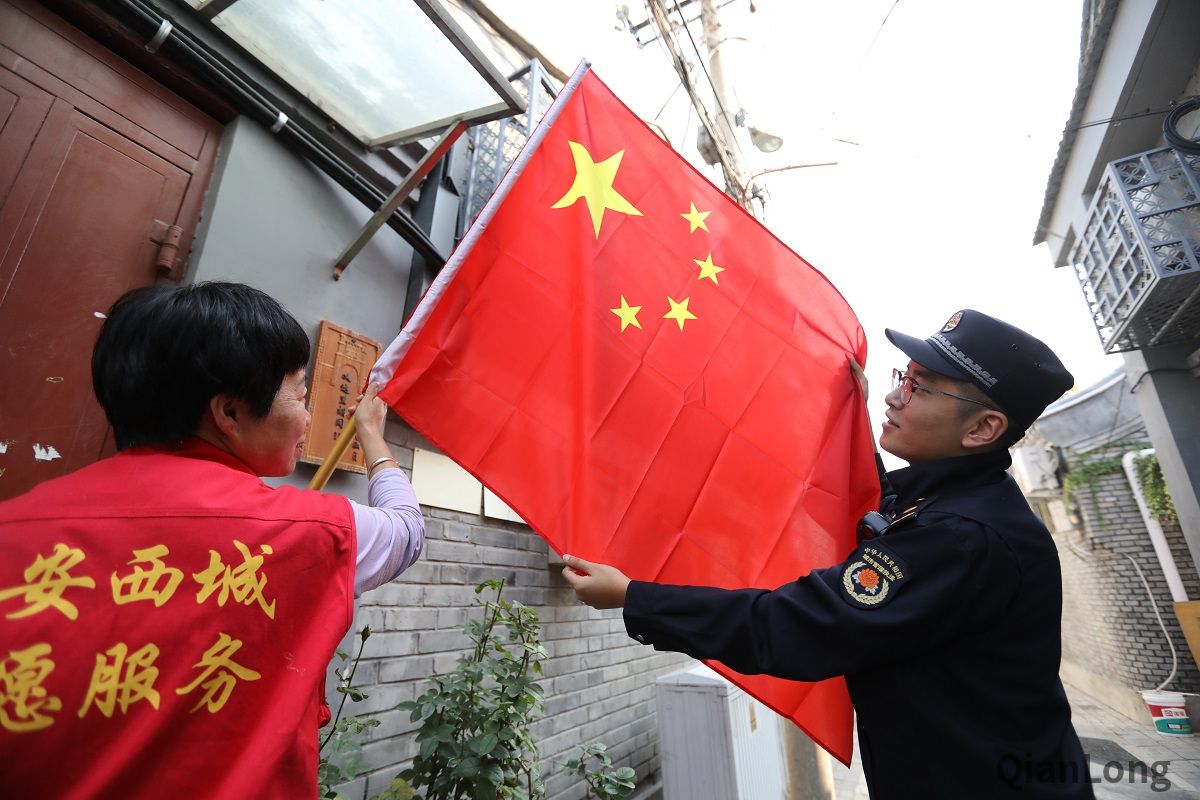 背街小巷里的环境秩序也是西城城管队员们在节期期间关注的重要工作内容之一，图为西长安街第一城管执法队队员在义达里社区帮助市民悬挂国旗。