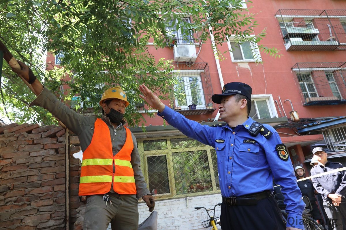 5月13日上午，展览路街道启动“街道吹哨，部门报道”工作机制，组织街道城管执法队、派出所、工商所、食药所、居委会，对月坛北街25号院55门北侧用于经营的老旧违建进行拆除，拆除面积15平方米。图为西城区展览路街道第二城管执法队队员与施工人员沟通拆除方案。