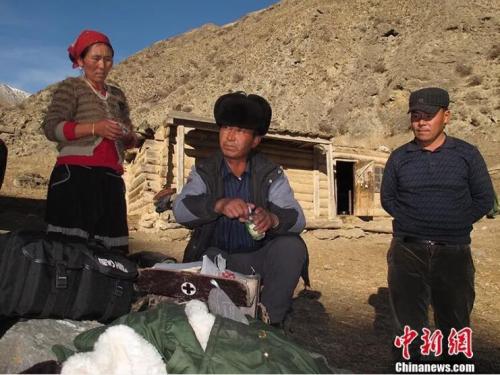 图为居马泰&middot;俄白克(中)在包扎墩牧区牧民发放药品。