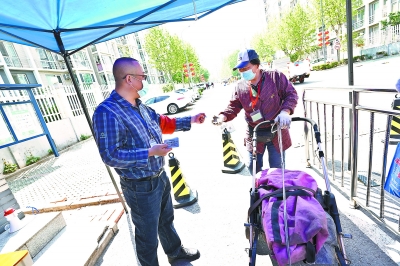 在回龙观街道新龙城4期北门值勤的社区工作人员王宜强正在为社区居民发放当天出入证。北京日报记者 方非摄  