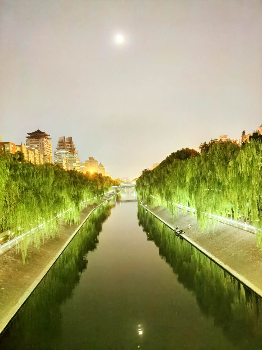 岸边路灯和水倒影着月亮,使河中显得格外美丽