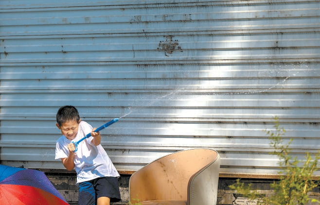 北京迎来今年首个高温日，最高气温超过35℃。头戴帽子、身穿防晒衣、手拿小风扇……市民“全副武装”出行，还有孩子在家门口玩水降温。本报记者 潘之望摄