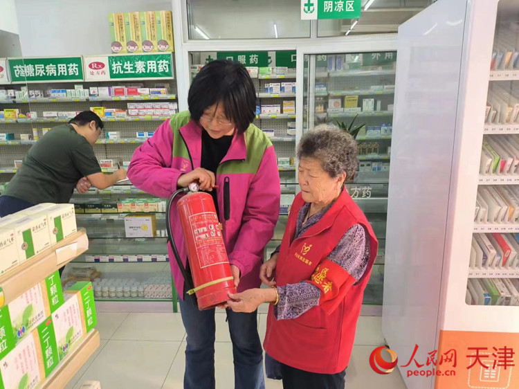 一位热心的&ldquo;河西大姐&rdquo;（右）在药店帮助工作人员检查灭火器。人民网记者 孙翼飞摄