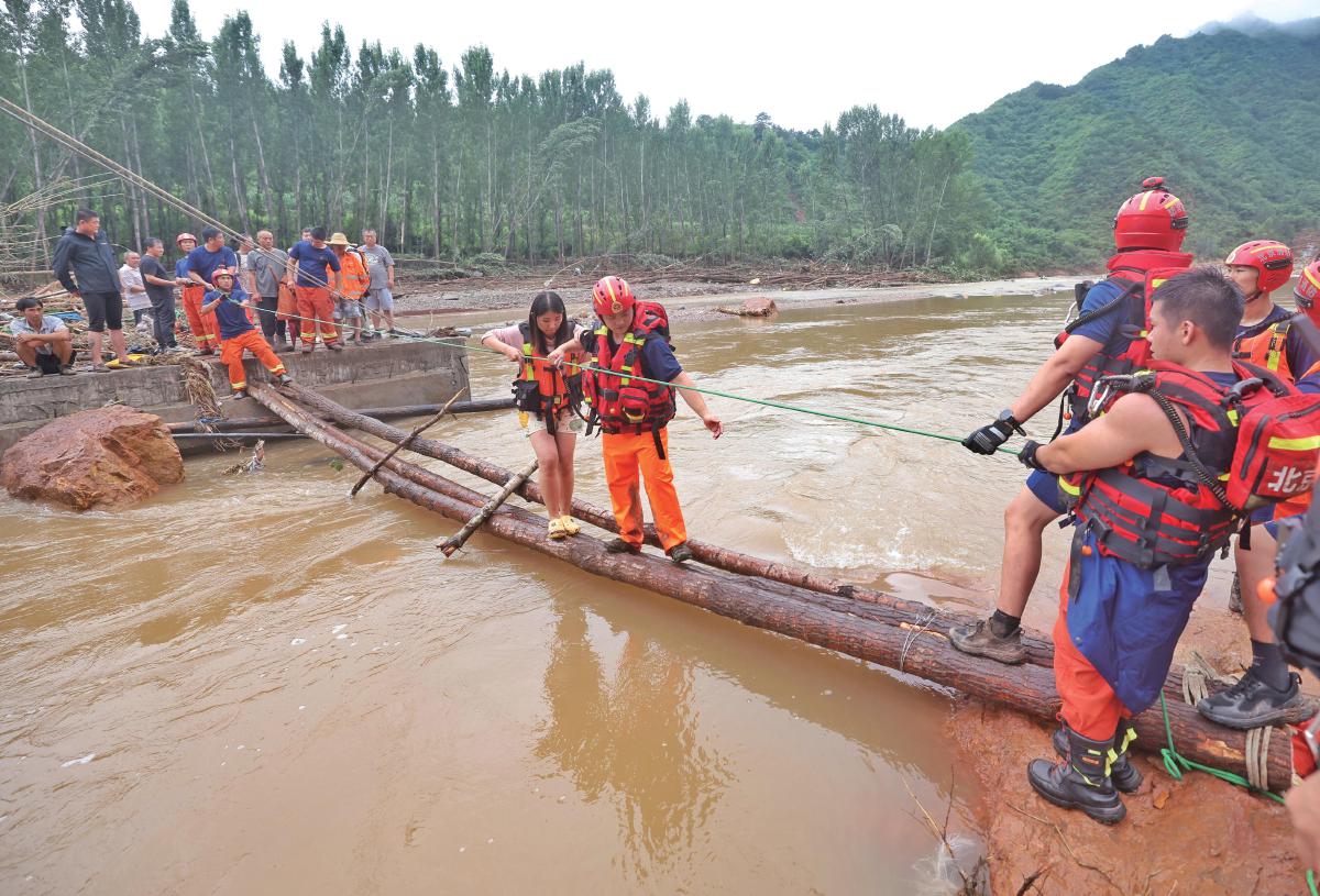 7月28日，北京怀柔区琉璃庙镇碾子湾村，消防员搭建浮桥转移被困人员。该村的桥被冲毁，怀柔区消防救援支队与来自海淀区的增援力量在断桥处，利用树木和绳索搭建起救援通道，成功将部分被困游客疏散至外部安置点。新京报记者 王贵彬 摄