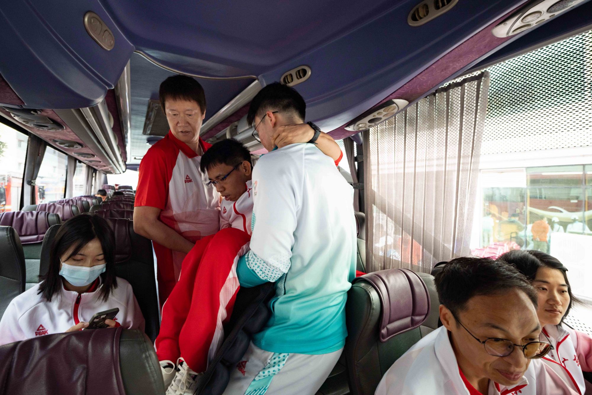 出发前,助教张健忠将行动不便的队员们逐一抱上大巴。 出发前,助教张健忠将行动不便的队员们逐一抱上大巴。